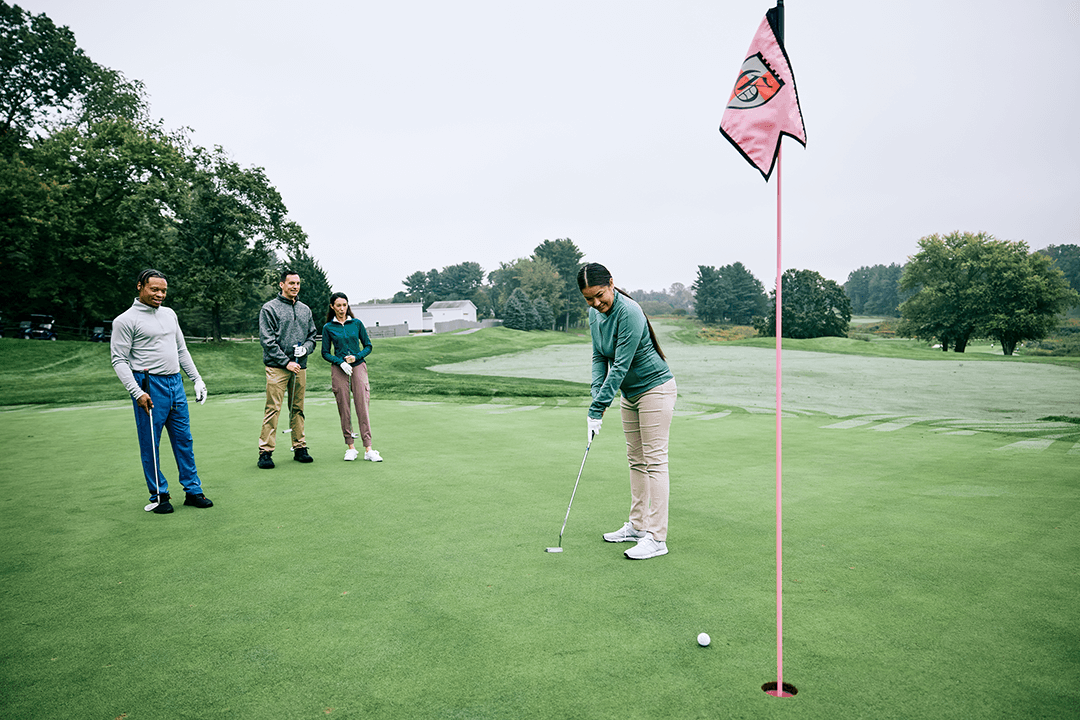Female golfer making a putt at Greystone Golf Course with three friends watching from the green.