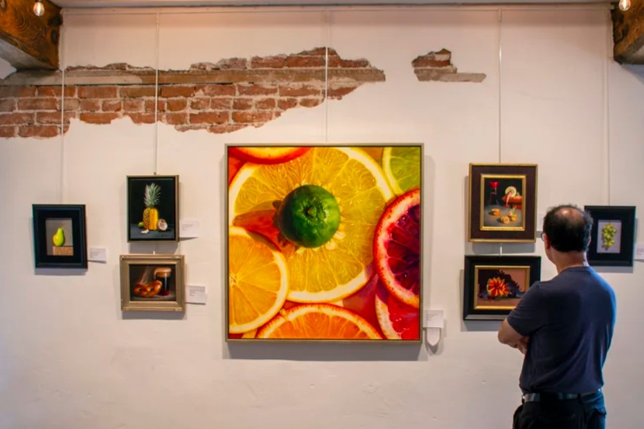 Man looking at a large painting of fruit on a wall in a gallery