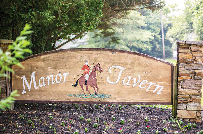 A wooden sign with "Manor Tavern" on it featuring a polo player on a horse.