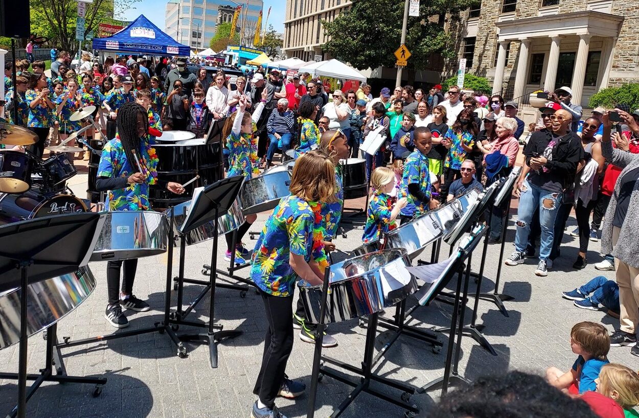 A large crowd watching a group of childres play the steel drums.