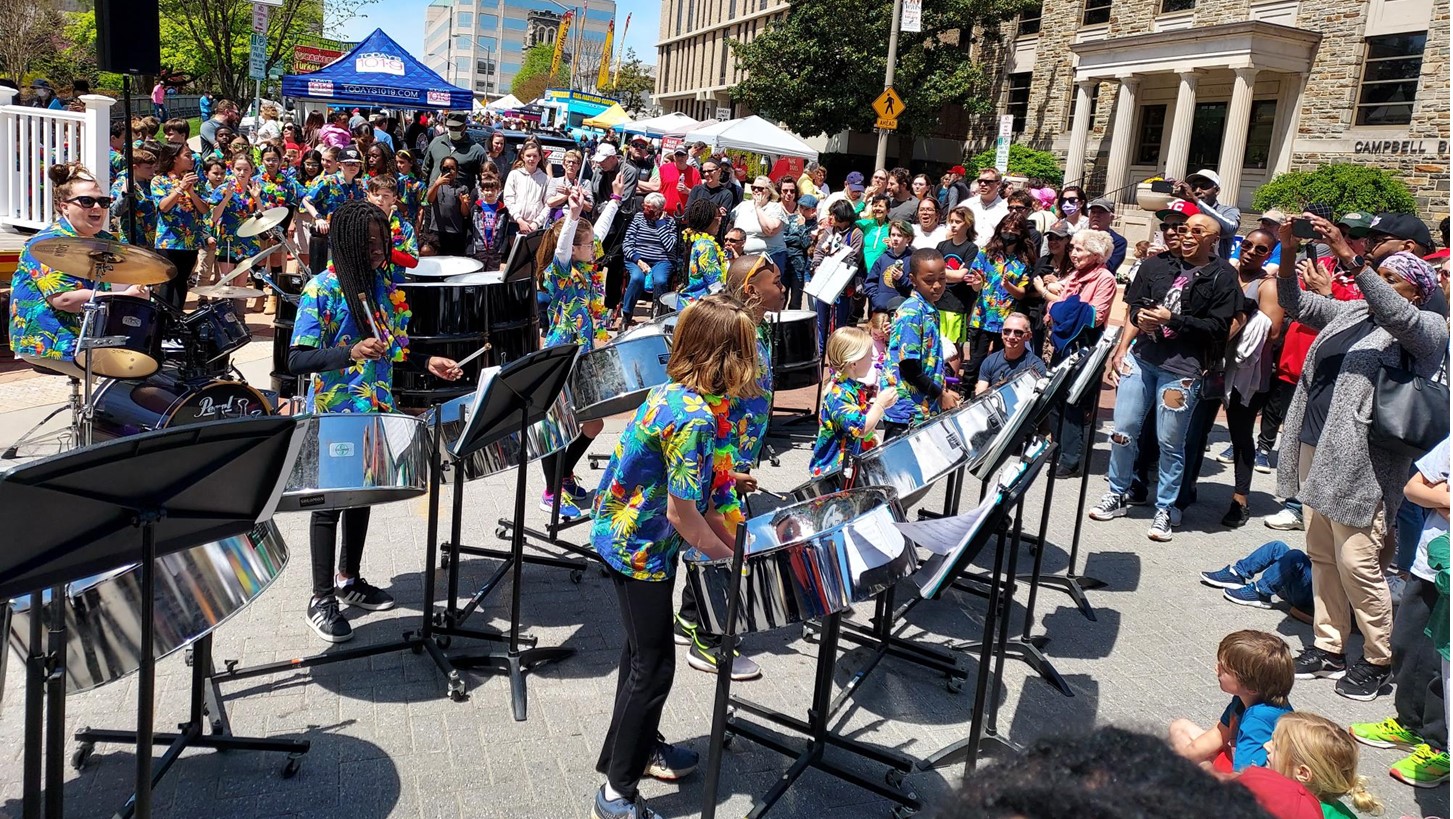 A large crowd watching a group of childres play the steel drums.