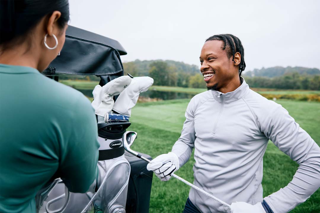 A male golfer smiling while standing next to a golf cart with a golf bag on the back.