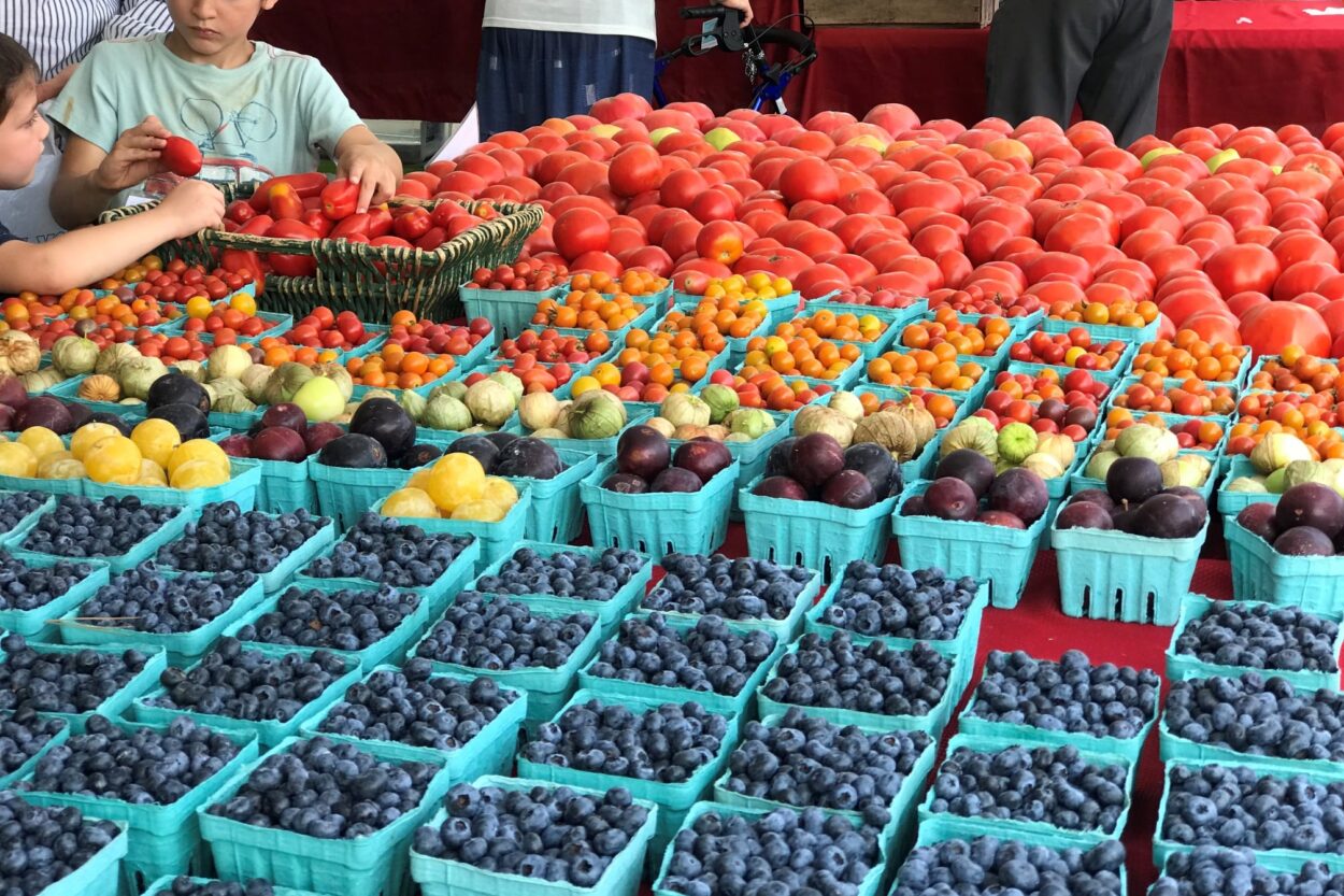 Rows of various fruits and vegetables in cartons on a table at the Pikesville Farmers Market.